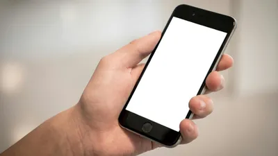 A hand holds a black smartphone with a blank white screen, ready for content.
