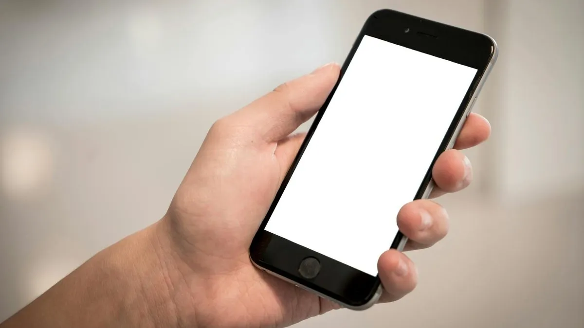 A hand holds a black smartphone with a blank white screen, ready for content.