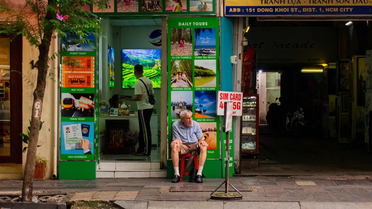 A senior man sitting outside a bustling tour office in Ho Chi Minh City, Vietnam.