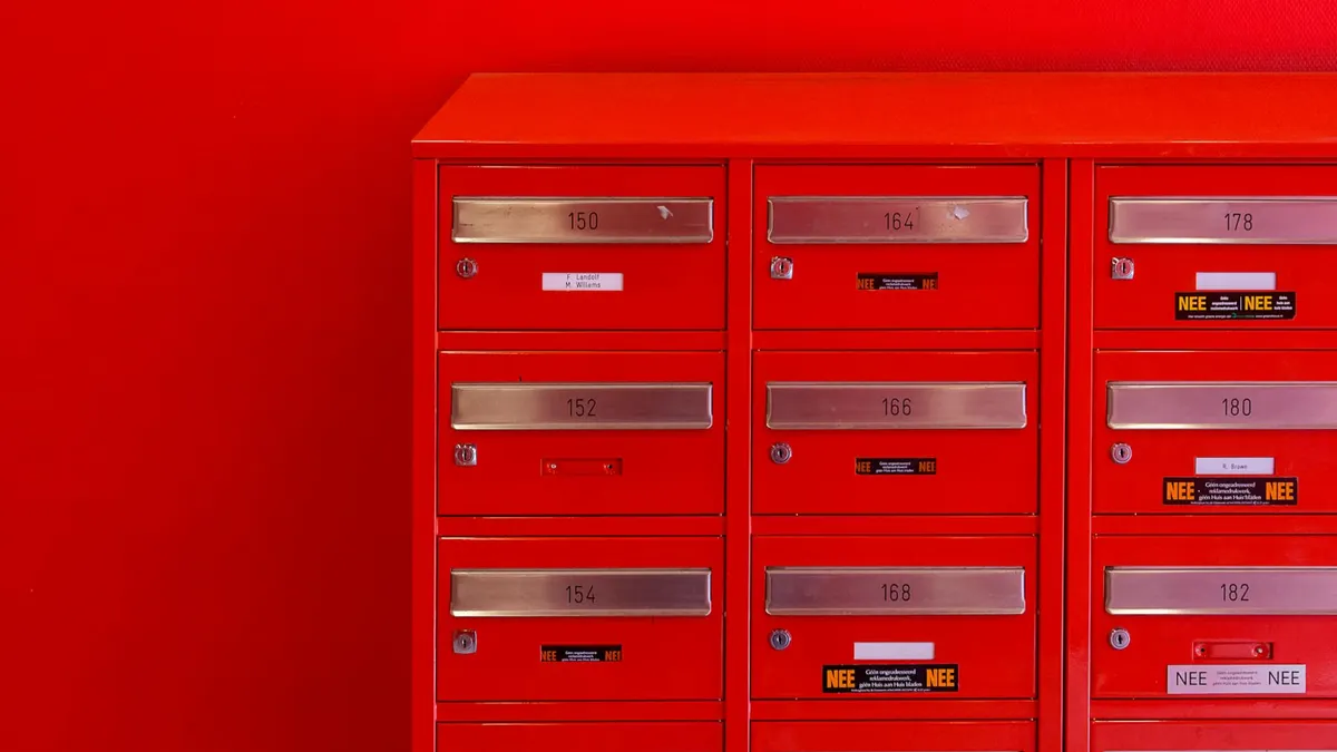A row of sleek red mailboxes with metallic number panels and keyholes against a red background.