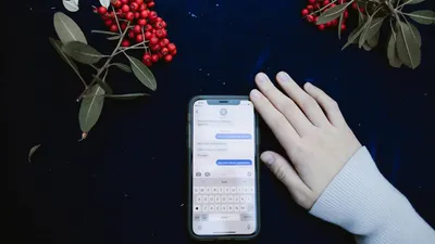 A hand beside a smartphone showing a text message conversation, surrounded by red berries.