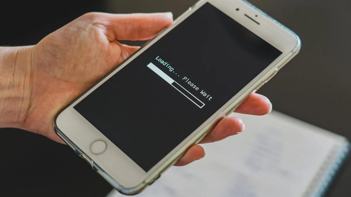 A hand holds a white smartphone displaying a 'Loading... Please Wait' message with a progress bar.