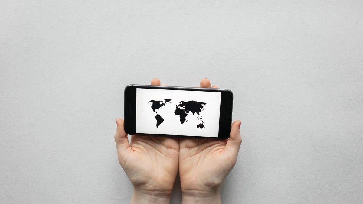 A pair of hands holds a smartphone horizontally, displaying a black and white world map.