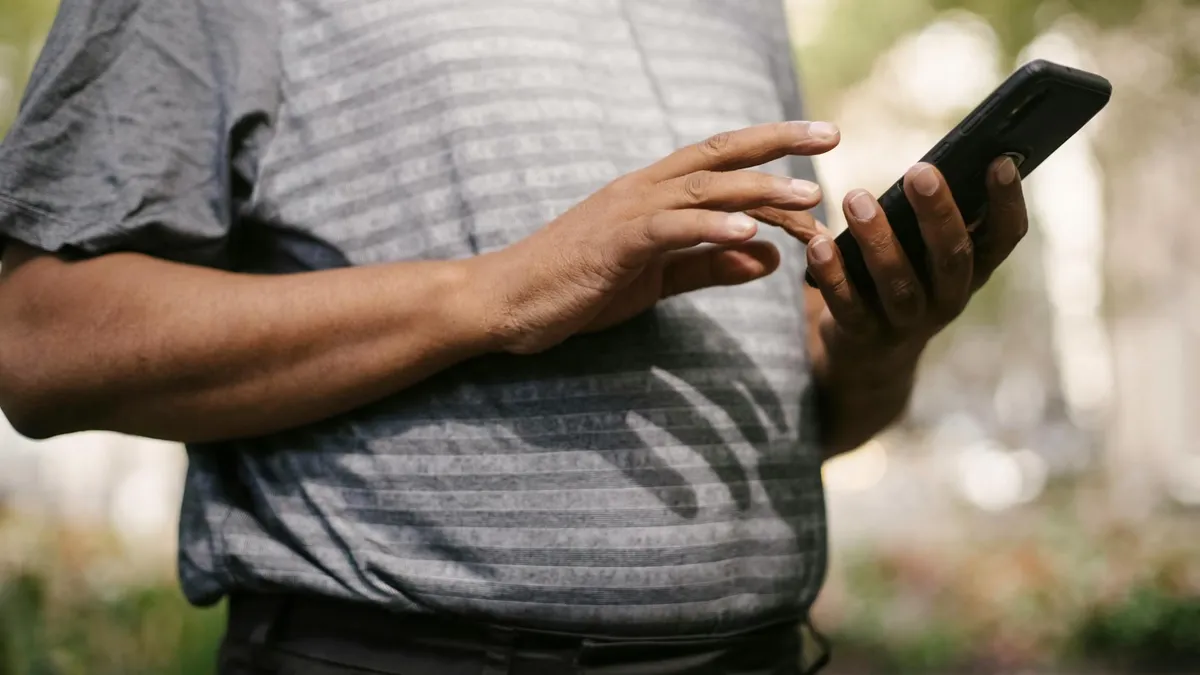 Crop anonymous male in casual clothes using smartphone on blurred background of street