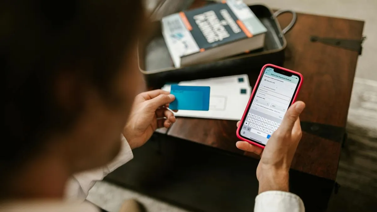 A person holds a smartphone in one hand and a blue credit card in the other.