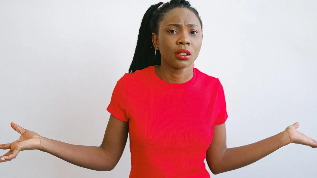 Young black woman in a red shirt with a confused expression. Perfect for emotive stock photo needs.