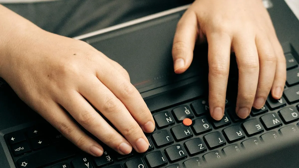 Close-up of hands typing on a laptop keyboard with a red pointing stick in the center.