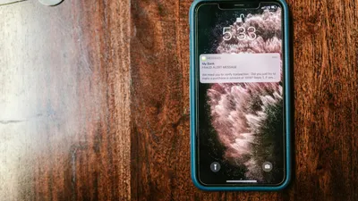 Close-up of a smartphone displaying a fraud alert message on a wooden table.