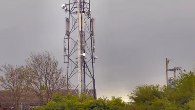 A telecommunications mast with multiple antennas and transmission equipment against a clear sky, representing shared mobile network infrastructure in the UK.