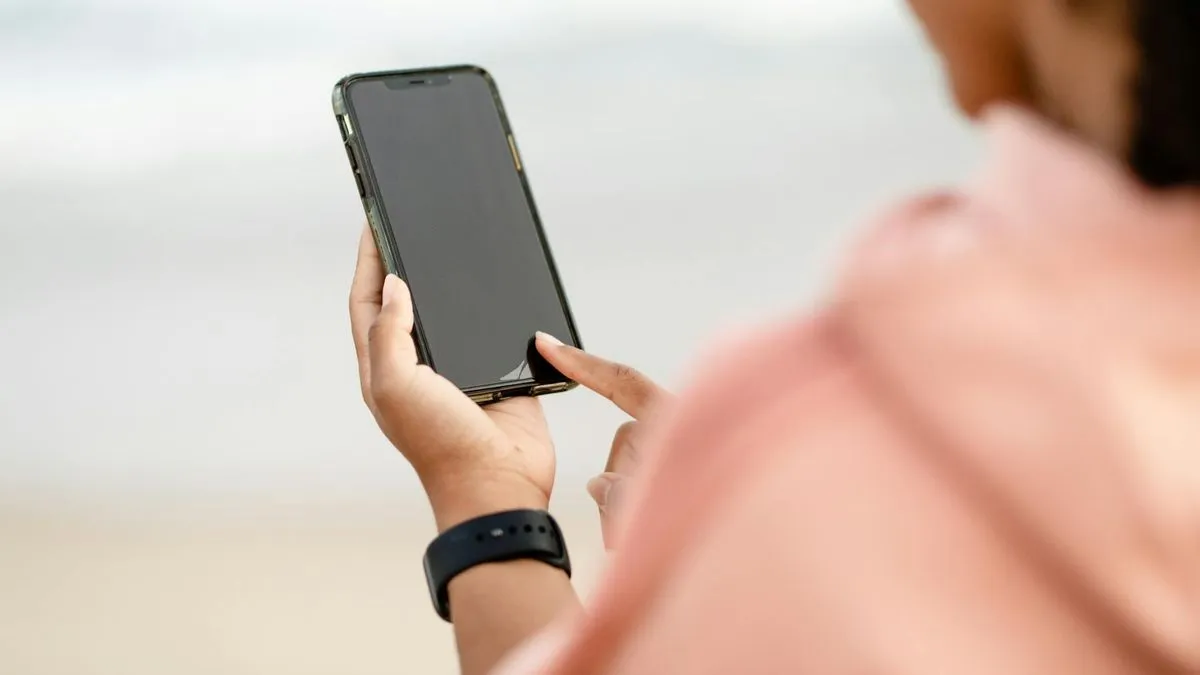A person in a peach top holds a black smartphone with their finger on the screen.