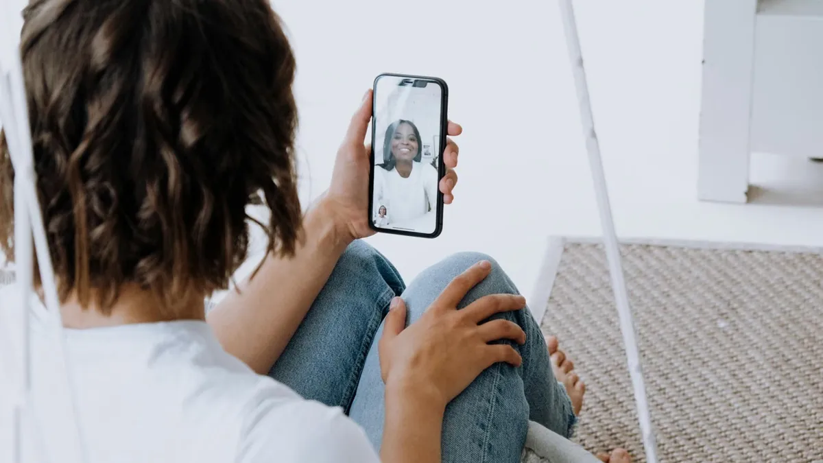 A young woman engages in a cheerful video call with a friend using a smartphone.