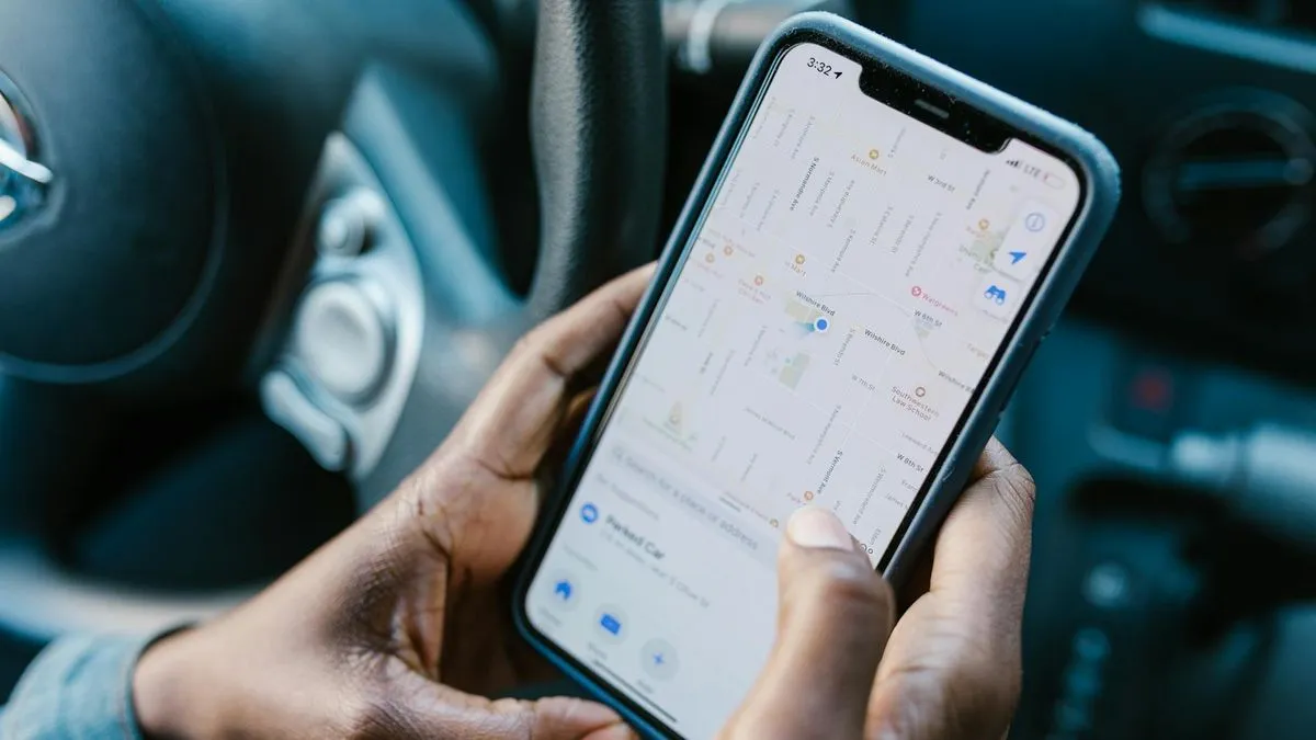 A person's hands holding a smartphone displaying a map application inside a car.