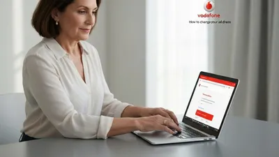 A woman with short brown hair and a white shirt sits at a desk, typing on a laptop.