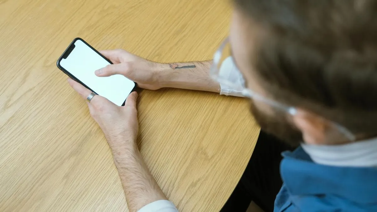 Overhead shot of a person holding a smartphone with a blank white screen over a wooden table.