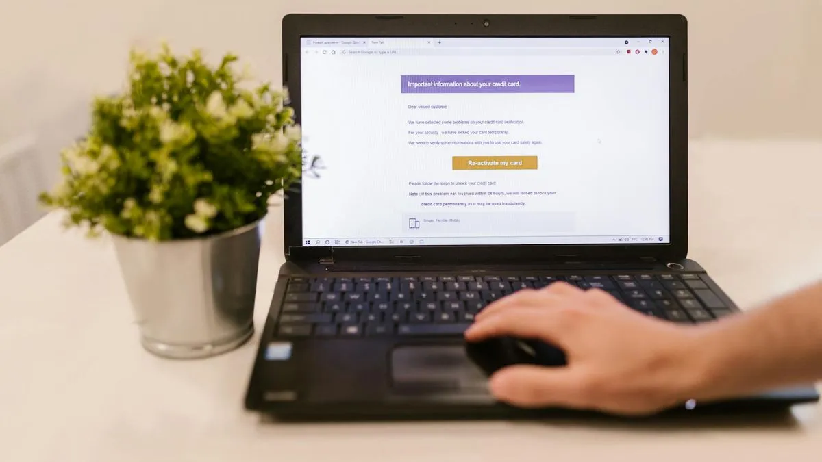 A person's hand using a mouse next to a laptop displaying an email interface.