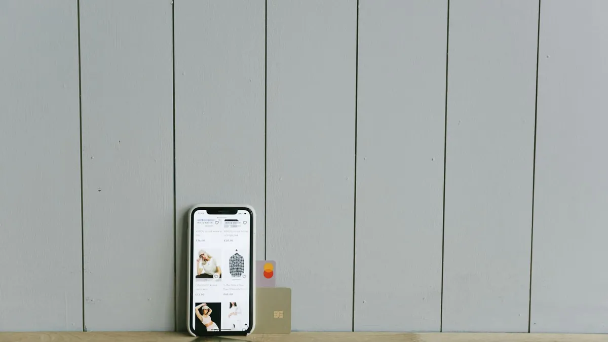 A smartphone displaying an ecommerce site with a credit card, set on a wooden surface, depicting online shopping.