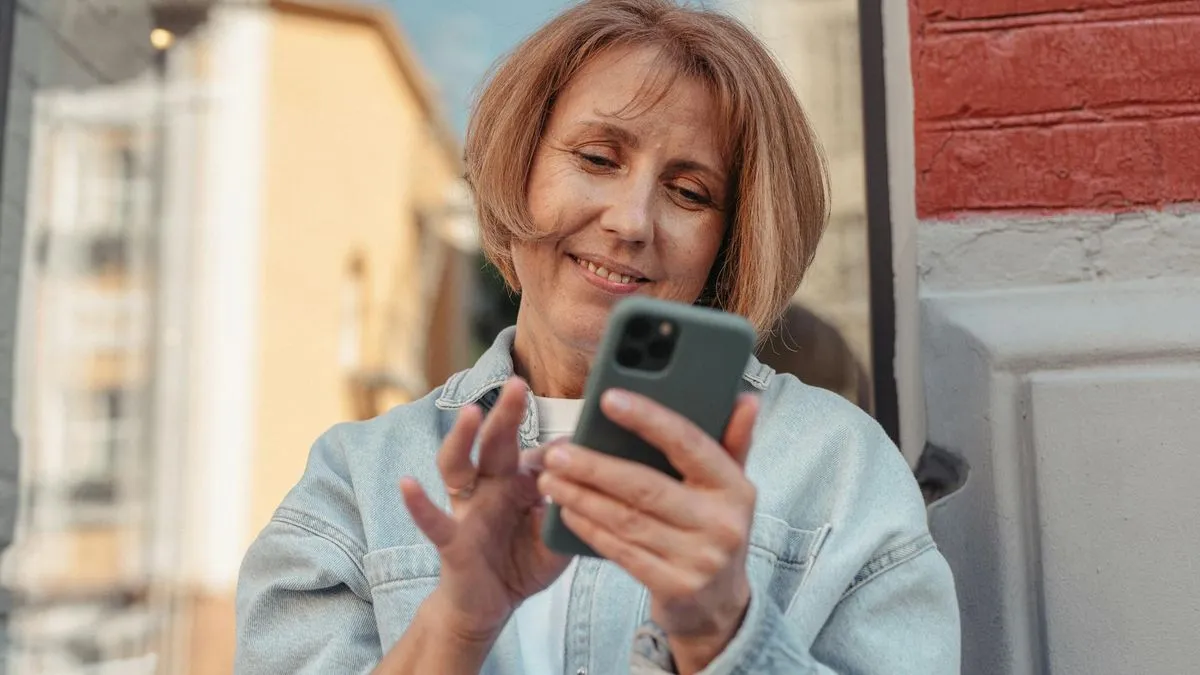 A smiling woman with short blonde hair looks at her smartphone outdoors.