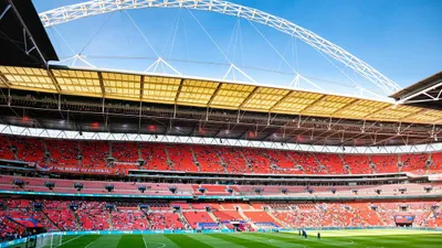 A wide shot of Wembley Stadium's interior, showing the green pitch, red seats, and iconic arch.