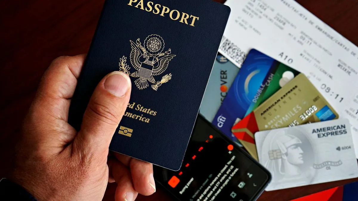 A hand holds a US passport, with credit cards, a phone, and a plane ticket visible.