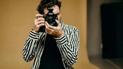 A man in a striped shirt holds a camera up to his face, ready to take a photo.