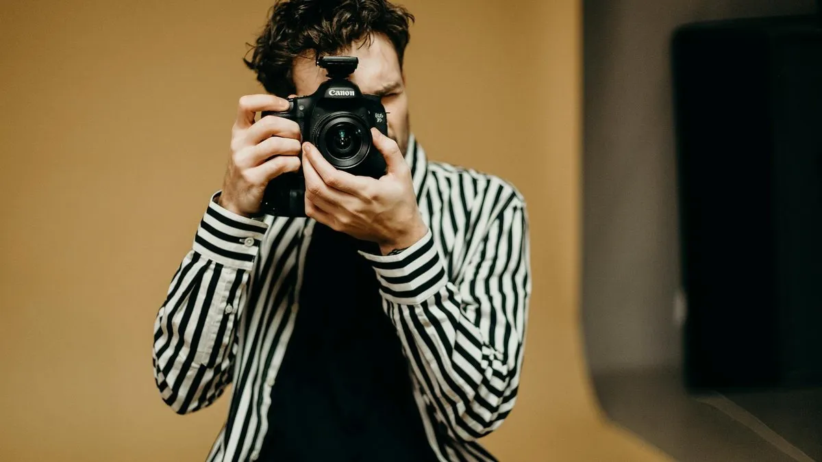 A man in a striped shirt holds a camera up to his face, ready to take a photo.