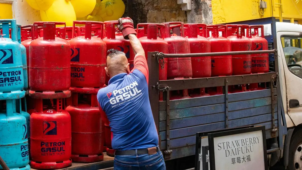 A man in a blue shirt loads red gas bottles onto a truck, with blue gas bottles stacked nearby.