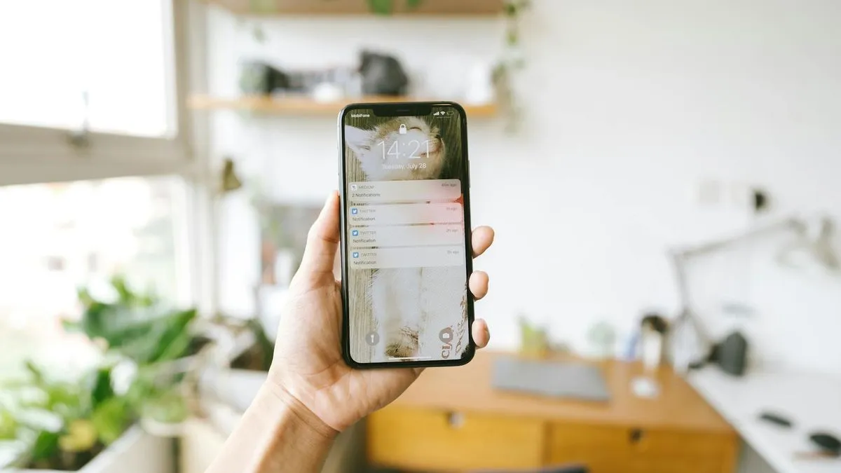 A hand holds a smartphone displaying a lock screen with notifications in a bright room.