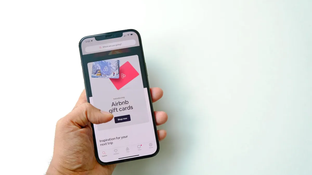 Close-up of a hand holding a smartphone displaying Airbnb gift cards on a white background.
