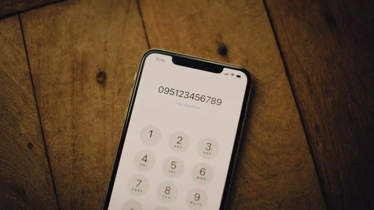 A smartphone displaying a phone number on its dial pad, resting on a wooden surface.