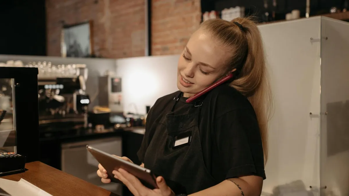 Young woman in café multitasks with a tablet and phone at the counter.