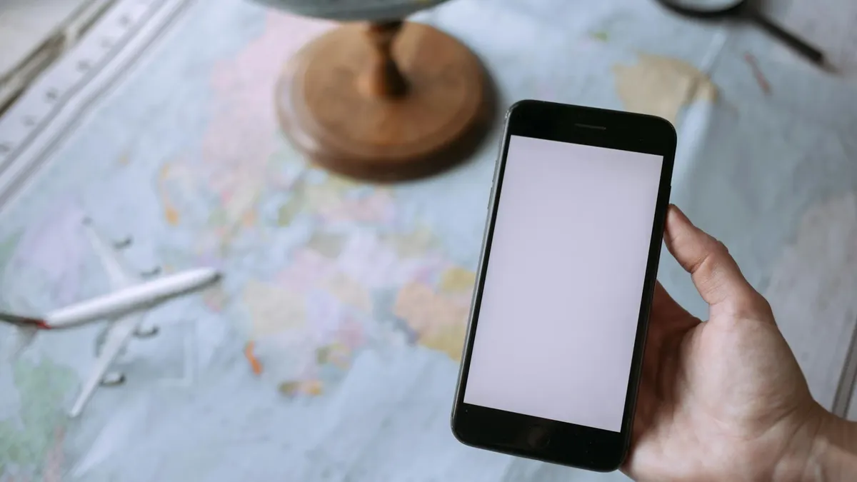 Hand holding smartphone over world map with globe and toy airplane, symbolizing travel planning.