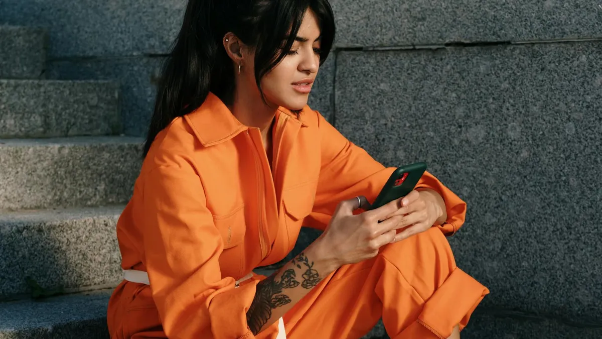 A woman sits on concrete steps, engrossed in her smartphone, showcasing modern urban style.