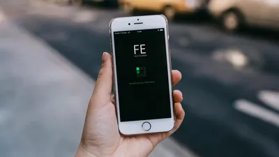 Close-up of a smartphone with an app on screen held by a person in an urban setting.