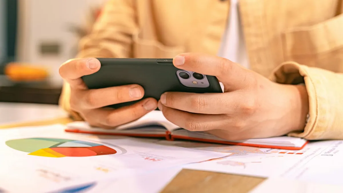 A business person checking their phone while working with graphs and charts on a desk.