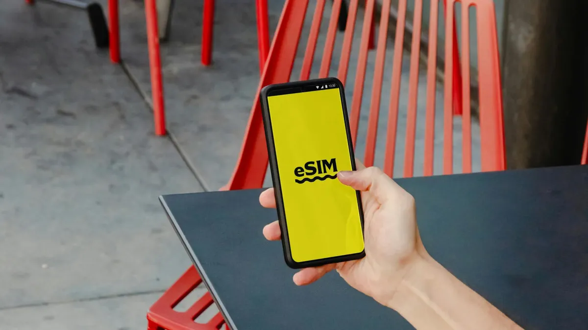 A person holding a smartphone displaying eSIM app screen, outdoors by red chair.