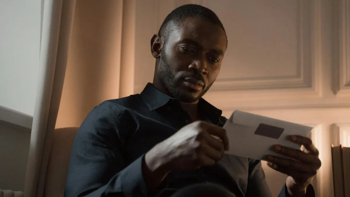 A man with a beard sits in a dimly lit room, opening a white envelope.