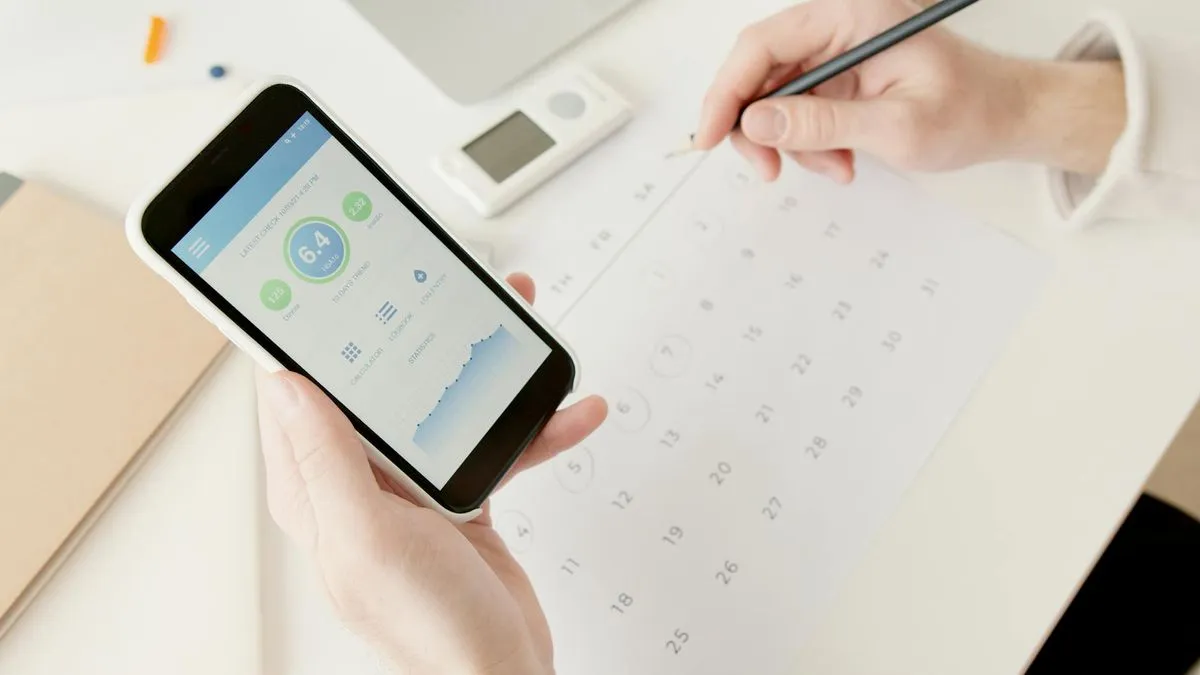 A person holding a smartphone displaying a data usage app, with a calendar and pencil on a desk.