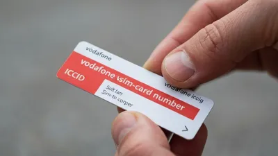 A person's hands holding a white and red Vodafone SIM card with 'SIM-card number' visible.