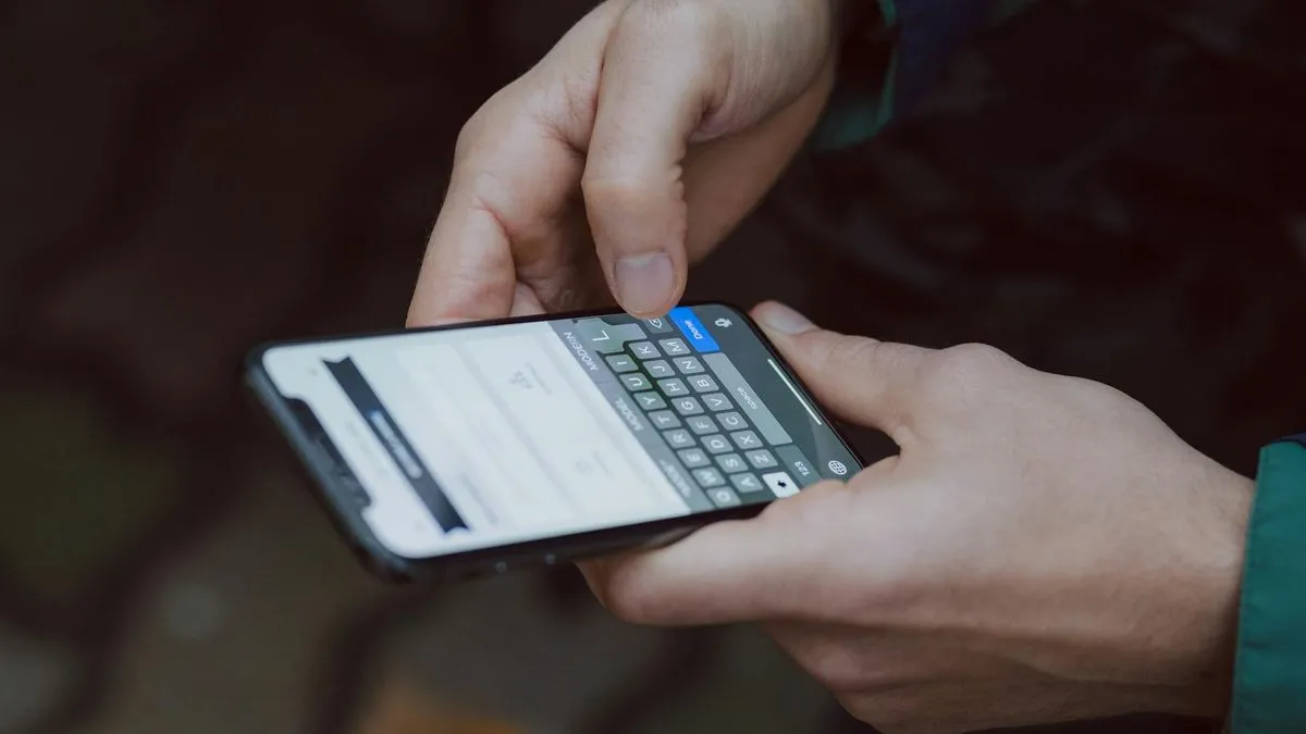 Close-up of hands typing on a smartphone screen with a keyboard visible.