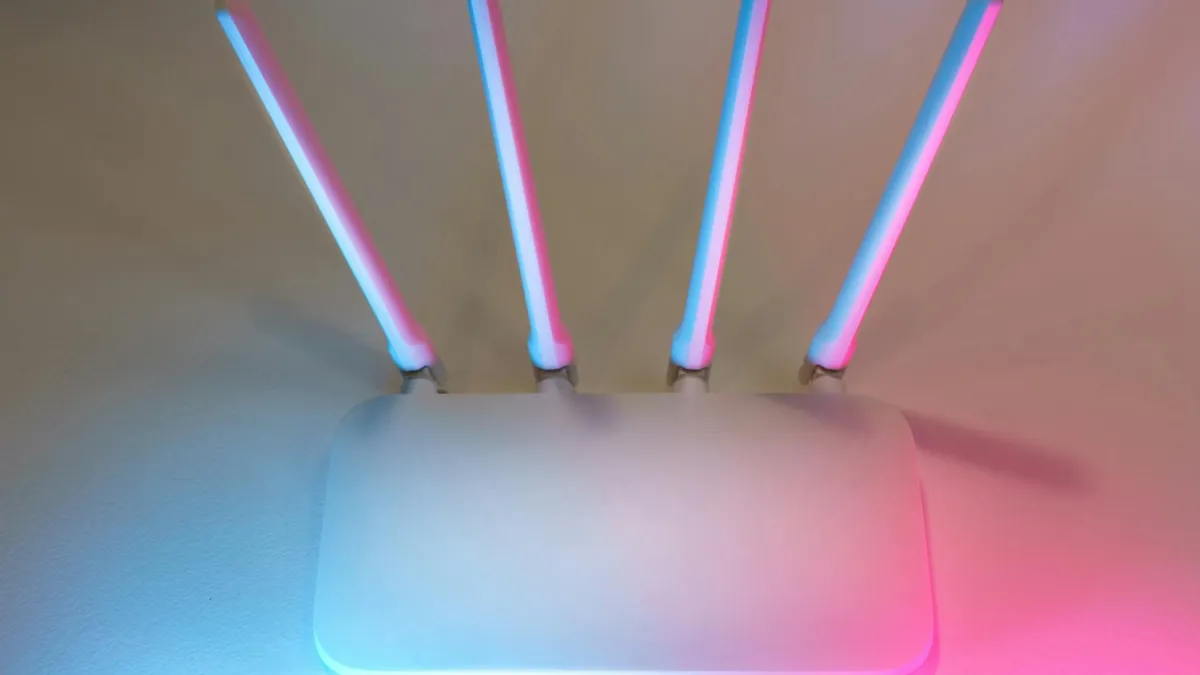 Sleek white wireless router with four antennas emitting soft blue and pink light.