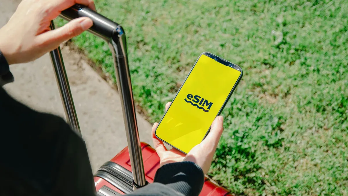 A person holds a smartphone showing an eSIM app while standing with luggage outdoors in Los Angeles.