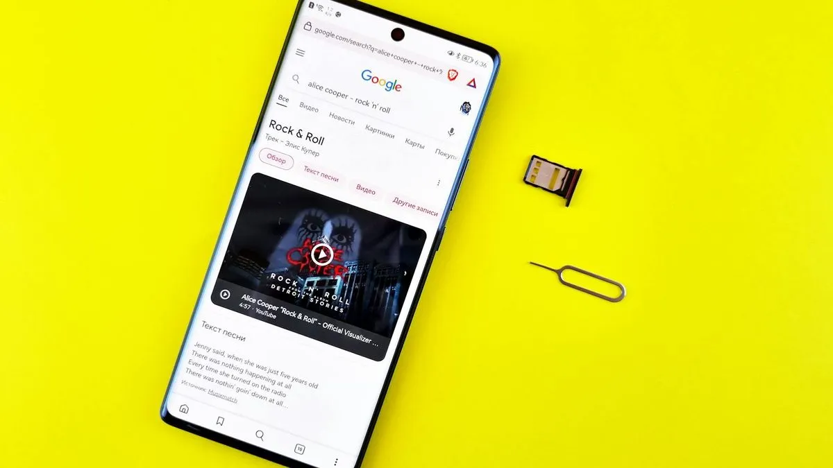 A smartphone on a yellow background with a SIM tray and SIM ejector tool next to it.