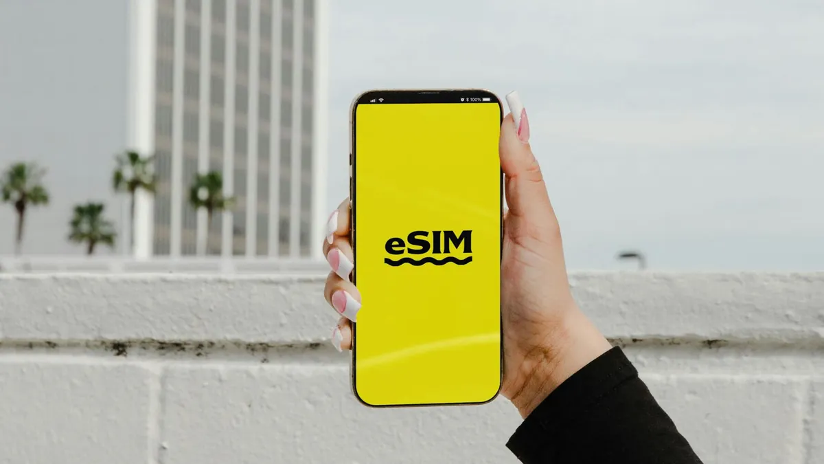 A hand holding a smartphone displaying 'eSIM' against an urban backdrop in Los Angeles.