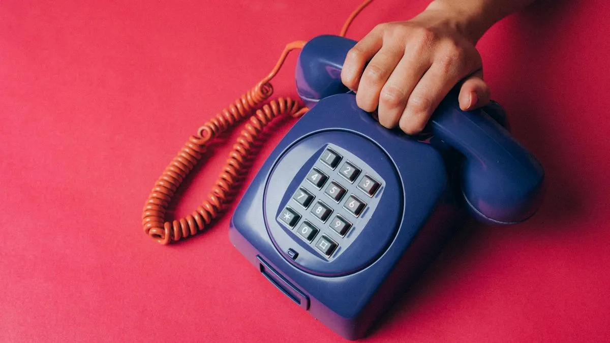 A hand holds the receiver of a blue push-button telephone on a bright pink background.