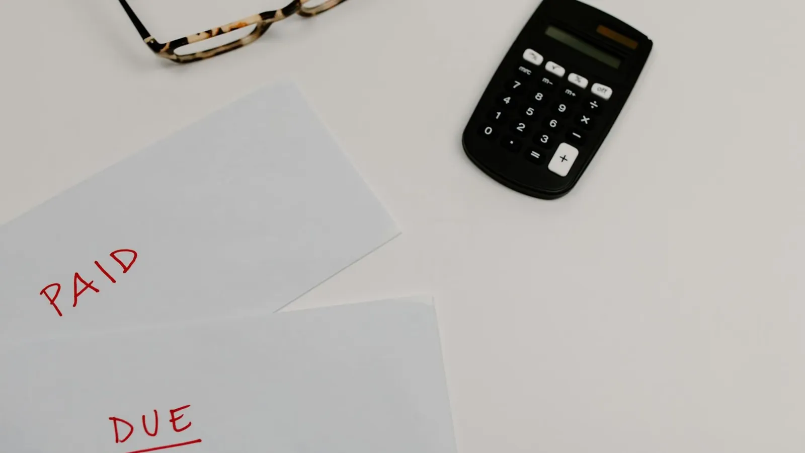 Top view of financial papers labeled 'Paid' and 'Due' beside a calculator and glasses.