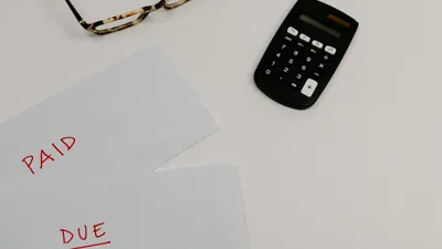 Top view of financial papers labeled 'Paid' and 'Due' beside a calculator and glasses.