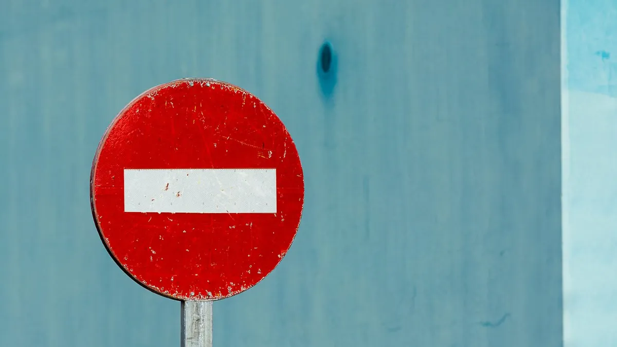 Close-up of a red no entry street sign with a blue wall background.