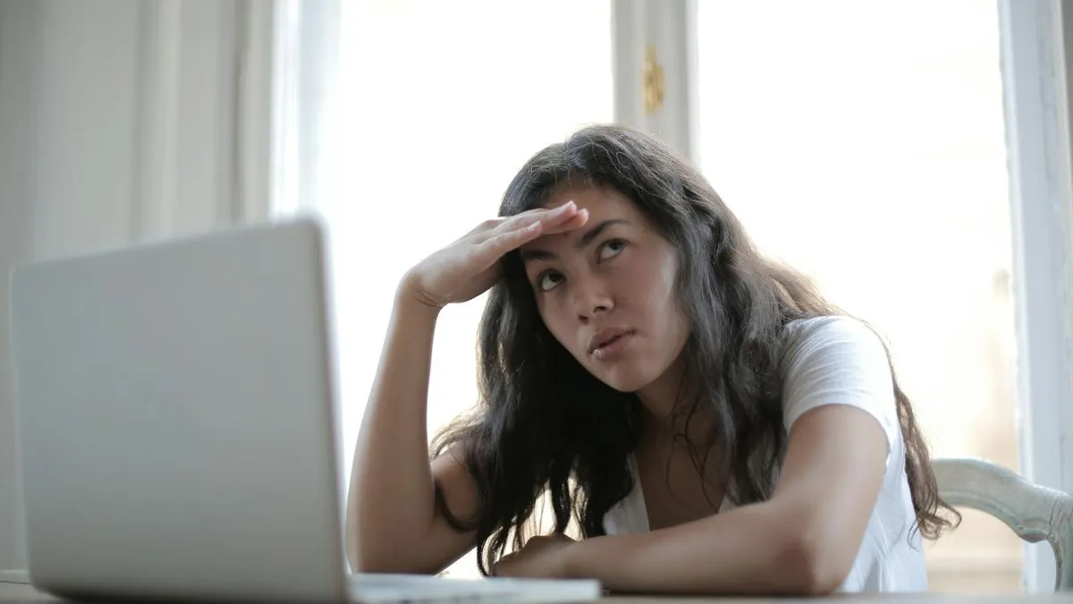 A woman with long dark hair looks frustrated while sitting in front of a laptop.
