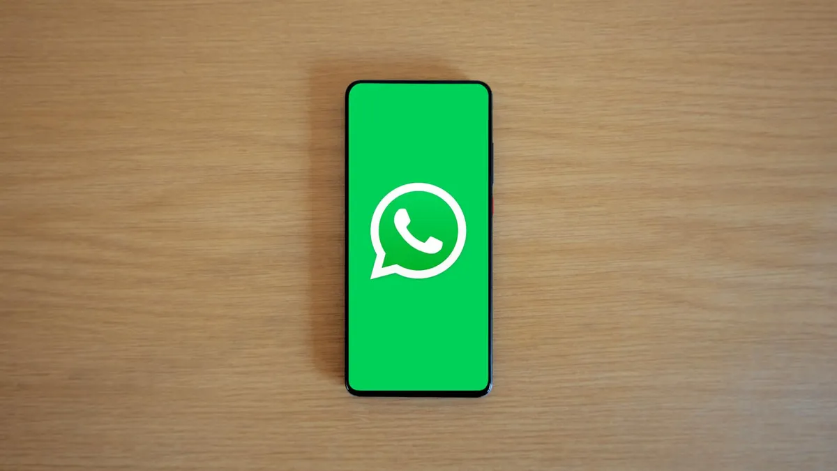 Top view of smartphone displaying WhatsApp logo on a wooden background, representing technology and communication.