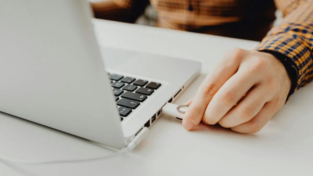 A person's hand inserting a white USB dongle into the side port of a silver laptop.